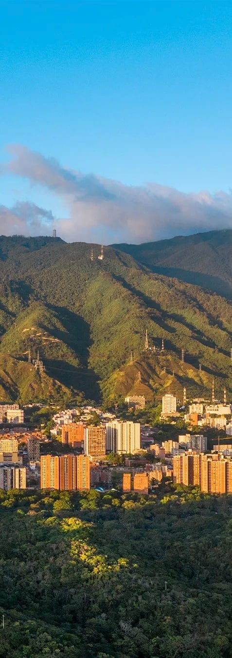 Aerial view of a city surrounded by green mountains with orange buildings and churches on hillsides under blue sky